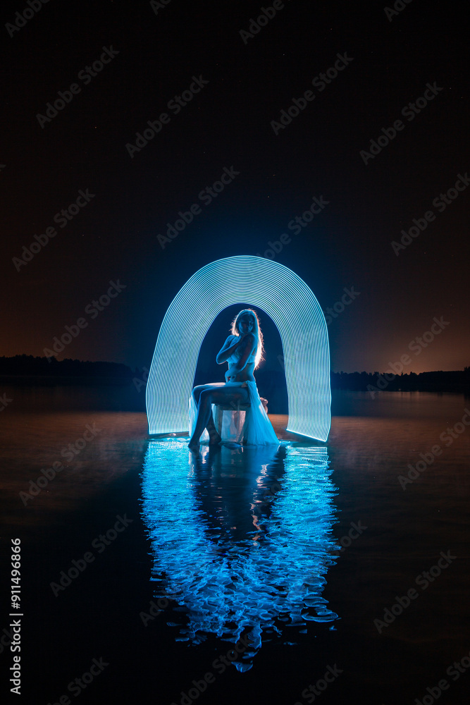 Young slim girl in white swimsuit posing in water at night with abstract blue light effect