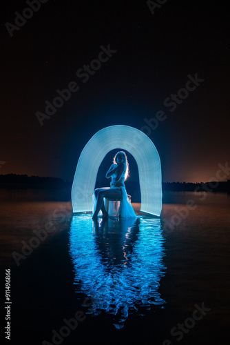 Obraz na płótnie Young slim girl in white swimsuit posing in water at night with abstract blue light effect w salonie