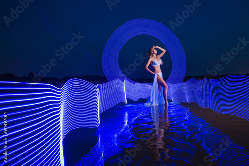 Obraz na płótnie Young slim girl in white swimsuit posing in water at night with abstract blue light effect w salonie