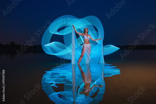 Obraz na płótnie Young slim girl in white swimsuit posing in water at night with abstract blue light effect w salonie