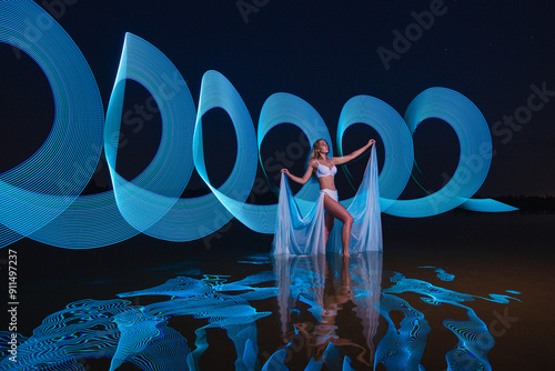 Obraz na płótnie Young slim girl in white swimsuit posing in water at night with abstract blue light effect w salonie