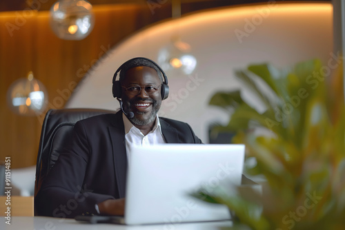 LGBT black man working as call center agent in modern bright office. African American gay or bi man smiling at camera while wearing headset, sitting in front of laptop and helping to customers. photo