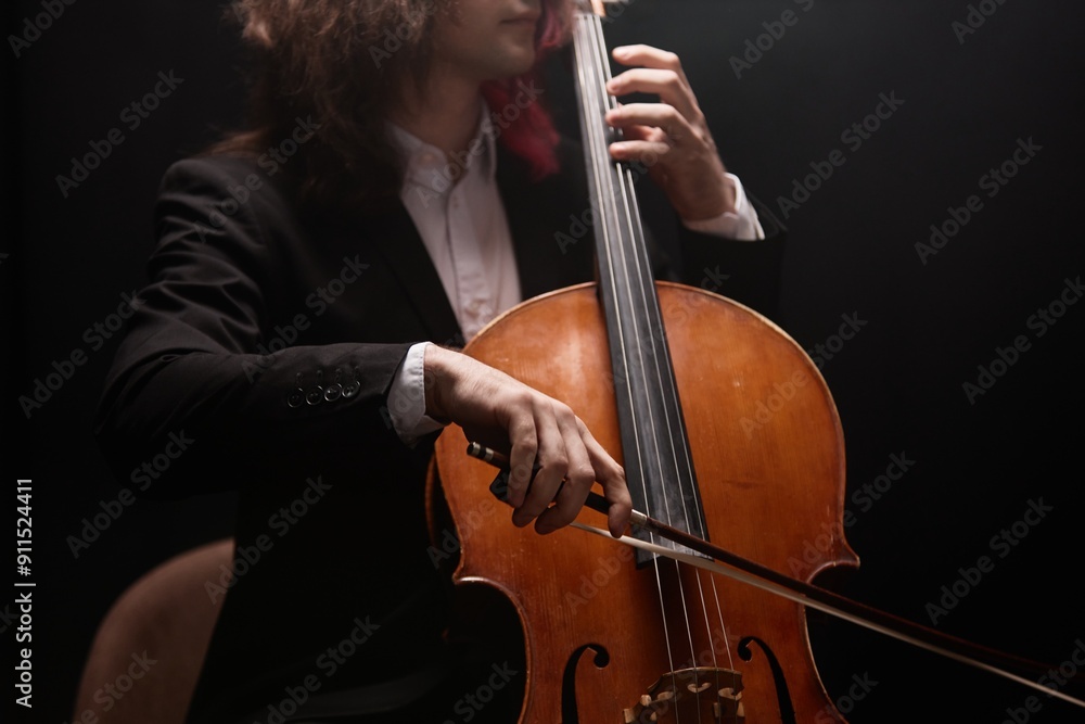 Cropped shot of unrecognizable male musician with long hair playing cello performing classical music on black background in dim lit recording studio Cropped shot of unrecognizable male musician with long hair playing cello performing classical music on black background in dim lit recording studio