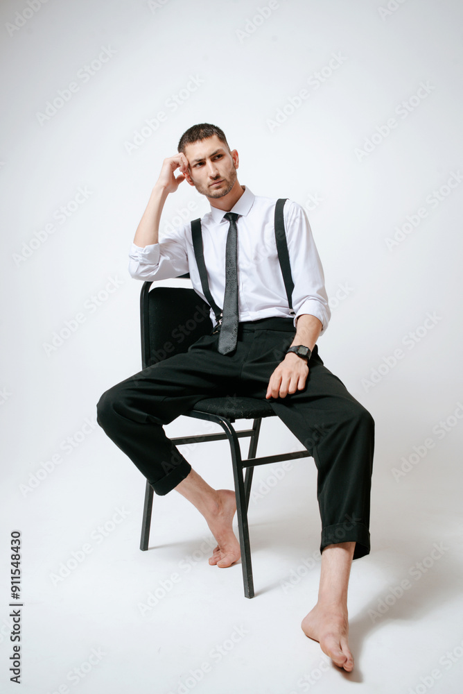 A man with white shirt and tie sits on a chair in studio. Barefoot A man with white shirt and tie sits on a chair in studio. Barefoot