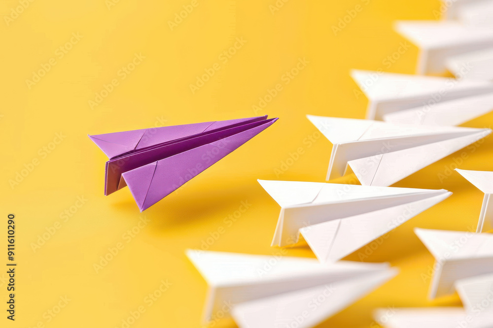 Fototapeta premium A striking image of a purple paper airplane standing out among white ones against a vibrant yellow background.
