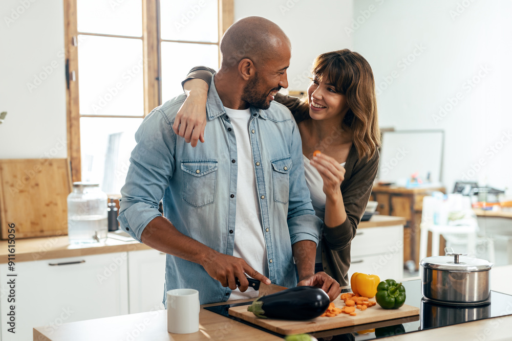 Beautiful and romantic couple hugging while cutting vegetables in the kitchen at home Beautiful and romantic couple hugging while cutting vegetables in the kitchen at home