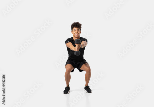 A man is engaged in a squat exercise while holding a dumbbell in each hand. This athletic endeavor takes place in a sleek indoor gym setting with bright ambient lighting