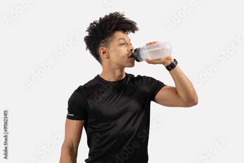 A young man is taking a break from his workout while staying hydrated. He is wearing a black athletic shirt and is focused on drinking from a clear water bottle. The background is blank photo