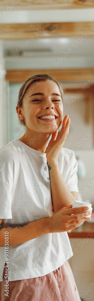 Happy woman applying hydrating moisturizer on her face sitting in bathroom. Home beauty routine Happy woman applying hydrating moisturizer on her face sitting in bathroom. Home beauty routine