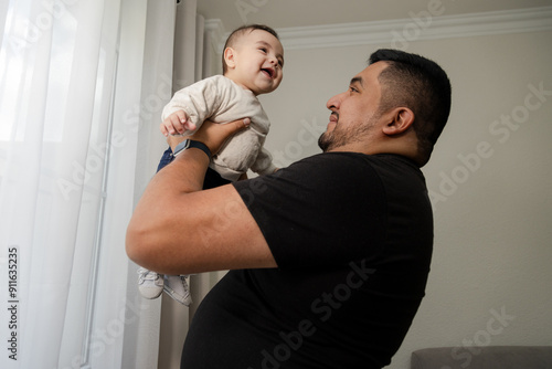 Father with his son smiling at home - young man enjoying his fatherhood with his 6 month old baby - single fatherYoung father holding his baby smiling in the living room of his house 