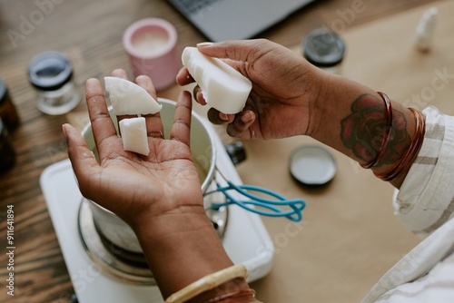 Close-up of hands crafting homemade soap with natural ingredients from above. This image captures intricate process of soap making with various tools present on wooden surface