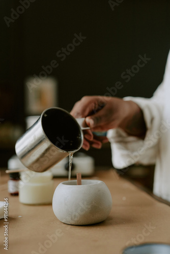 Person pouring wax from a metal container into a stone candle mold, crafting homemade candles in serene environment, creating an artisanal product using traditional methods photo