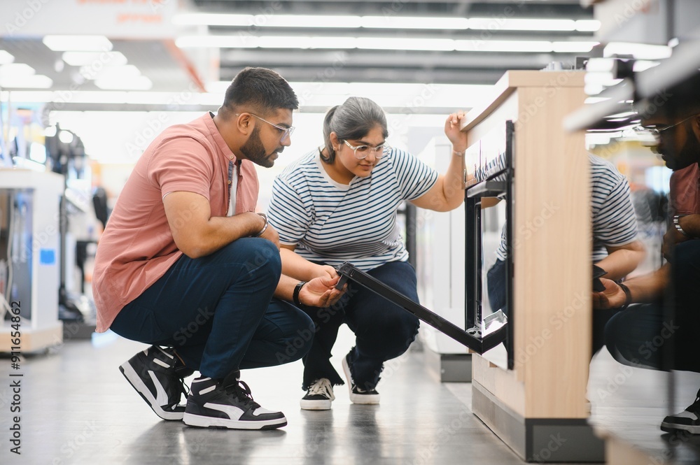 Couple of young customers looking at buildin cookers in domestic appliances shop Couple of young customers looking at buildin cookers in domestic appliances shop