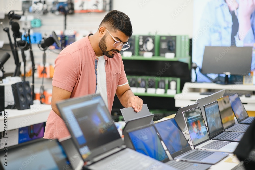 © Serhii - A male buyer looks at laptops in the computer department of the electronics store © Serhii - A male buyer looks at laptops in the computer department of the electronics store