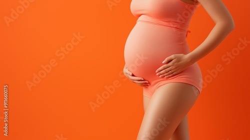 Pregnant woman in orange clothing cradling belly against bright orange background, symbolizing health and vitality. photo