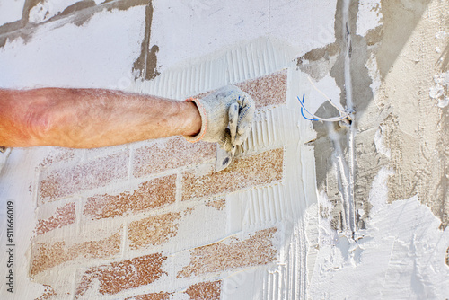 Brick cladding, also called brick veneer is attached to exterior of house made of aerated concrete blocks, construction worker uses tile adhesive. photo