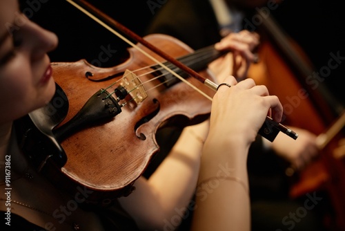Close up on hand of unrecognizable female orchestra musician playing violin with bow during concert on stage, focus on hand and tailpiece