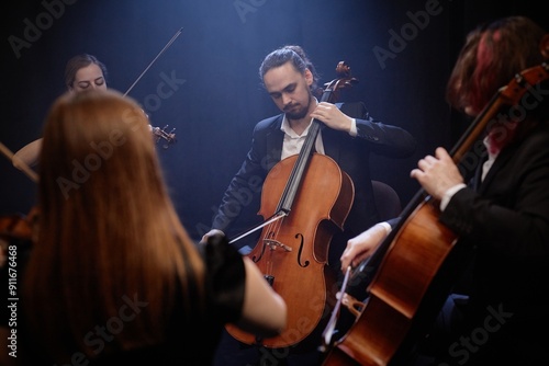 Bild auf Leinwand Young male musician in black suit playing cello with professional string quartet