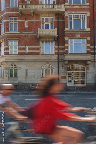 A motion-blurred image of cyclists riding past a red brick building