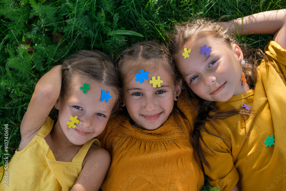 Children lie on the grass in the park with their faces decorated with colored puzzles. World Awareness Day about Autism. Children lie on the grass in the park with their faces decorated with colored puzzles. World Awareness Day about Autism.