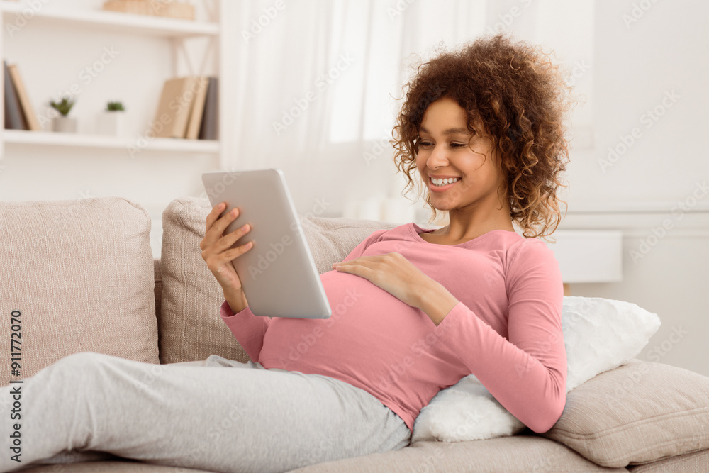Fototapeta premium Order kids clothes. Happy pregnant girl using tablet, browsing internet at home