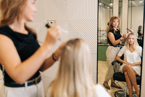 Back view of woman hairstylist applying peeling purifying and soothing cosmetics product to scalp using cotton swabs. Reflection on mirror of blonde female having professional hair beauty treatment.