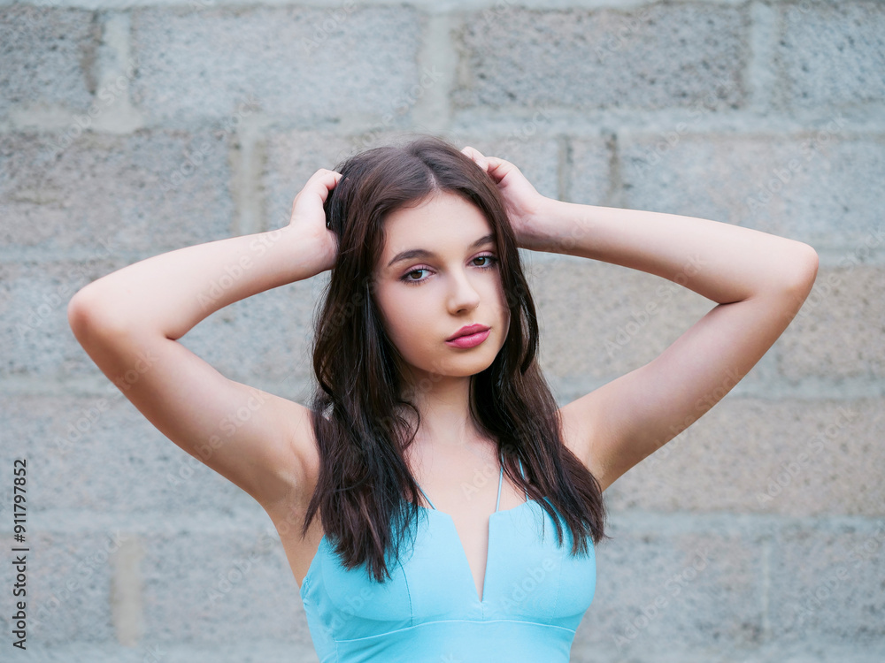 A woman in a blue dress is standing in front of a brick wall. Concept of elegance and sophistication, as the woman is dressed in a beautiful blue dress and poses confidently. A woman in a blue dress is standing in front of a brick wall. Concept of elegance and sophistication, as the woman is dressed in a beautiful blue dress and poses confidently.