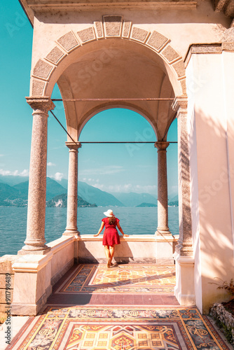 A woman in a red polka dot dress poses with a view of Lake Como from the botanical garden of Villa Monastero, Varenna, Italy. 