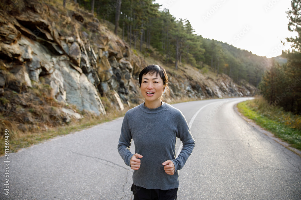 Smiling asian athlete jogging on mountain road against sky