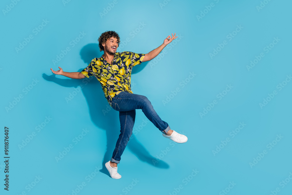 Full size photo of positive man dressed print shirt jeans raising arms up dancing look empty space isolated on blue color background Full size photo of positive man dressed print shirt jeans raising arms up dancing look empty space isolated on blue color background