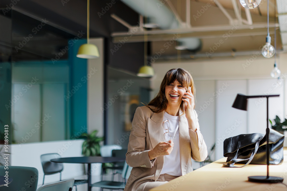 © BONNINSTUDIO/Stocksy - Happy businesswoman talking on phone in modern office space © BONNINSTUDIO/Stocksy - Happy businesswoman talking on phone in modern office space