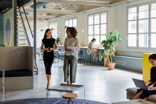 Two businesswomen walking and discussing in modern open space office