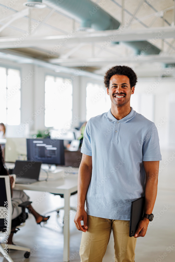Manager holding laptop standing in open plan office Manager holding laptop standing in open plan office
