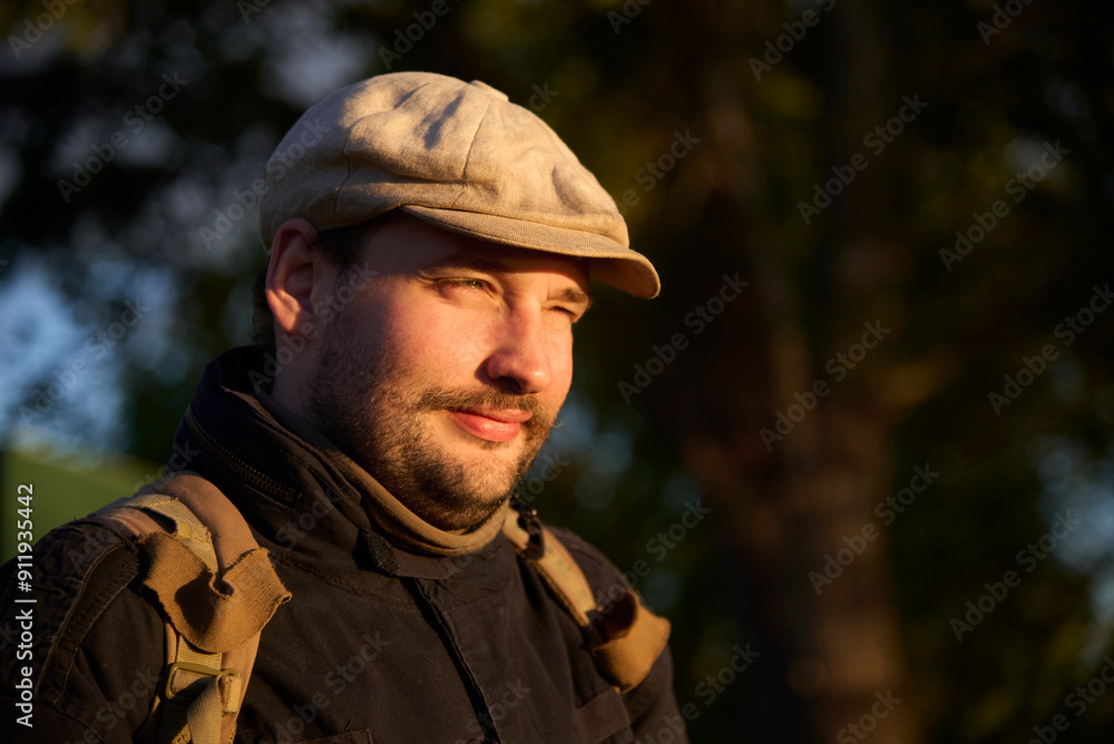 Portrait of a young man wearing a beret looking towards the sun at sunset without sunglasses, you can see from his gesture that the light is bothering his eyes, but he is smiling. Portrait of a young man wearing a beret looking towards the sun at sunset without sunglasses, you can see from his gesture that the light is bothering his eyes, but he is smiling.