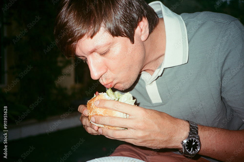 A man eating a burger in the evening A man eating a burger in the evening