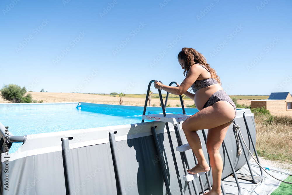 Pregnant woman climbing swimming pool ladder in summer Pregnant woman climbing swimming pool ladder in summer