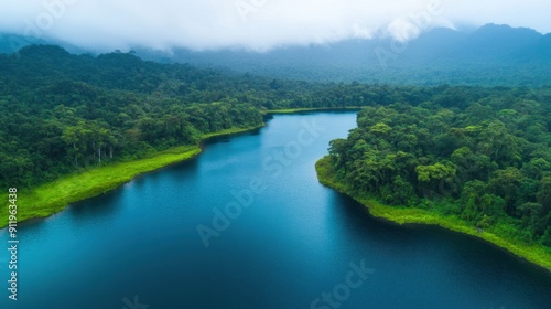 A tranquil mountain lake reflects the dense forest as mist gently rolls in with the dawn
