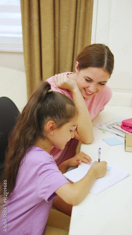 A caring mother helps her daughter with her homework in a warm, cozy children's room at a desk filled with colorful stationery and teaching aids. A caring mother helps her daughter with her homework in a warm, cozy children's room at a desk filled with colorful stationery and teaching aids.