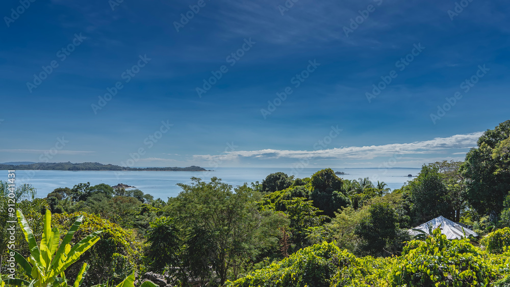 Beautiful sea bay. Tiny islands are visible in the ocean. Mountains on the horizon. Blue sky, clouds. There is lush green vegetation in the foreground. The top of the gazebo roof among the greenery. Beautiful sea bay. Tiny islands are visible in the ocean. Mountains on the horizon. Blue sky, clouds. There is lush green vegetation in the foreground. The top of the gazebo roof among the greenery.