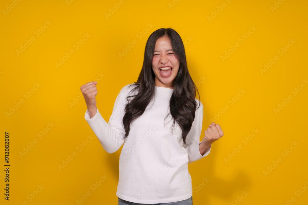 Young woman is making a winning gesture with a big smile while standing on a yellow background Young woman is making a winning gesture with a big smile while standing on a yellow background