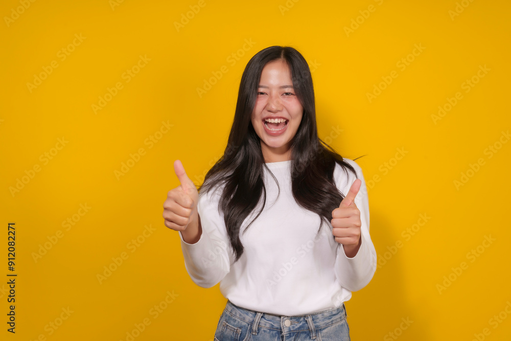 Young woman with long black hair is giving a double thumbs up gesture and smiling on a yellow background Young woman with long black hair is giving a double thumbs up gesture and smiling on a yellow background