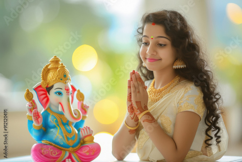 young Indian woman wearing cream colour dress and prayer, and side table a big colourful and beautiful lord Ganesha statue. photo