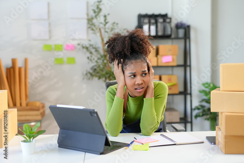 Young entrepreneur is feeling stressed while working at her desk, surrounded by boxes of products