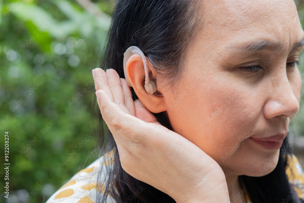Side view of attractive Asian adult woman with hearing aid over nature background. Side view of attractive Asian adult woman with hearing aid over nature background.