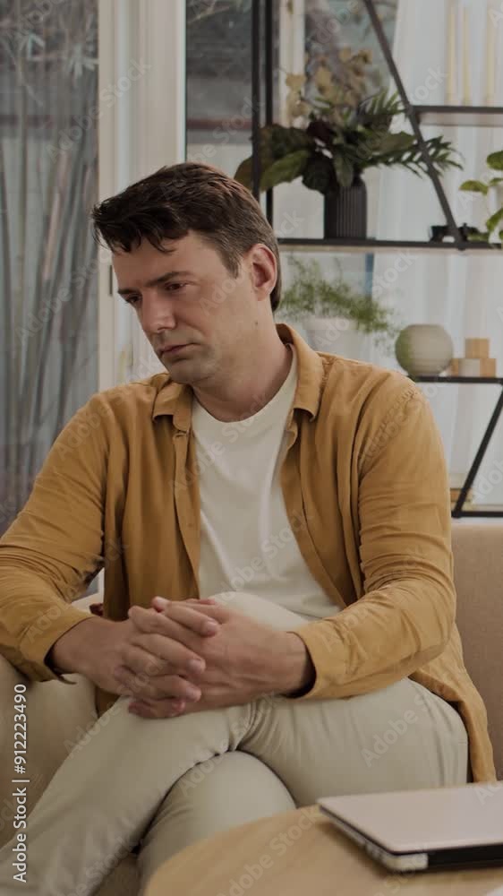 Vertical shot of middle-aged Caucasian man thinking about problems in his business when sitting on sofa Vertical shot of middle-aged Caucasian man thinking about problems in his business when sitting on sofa