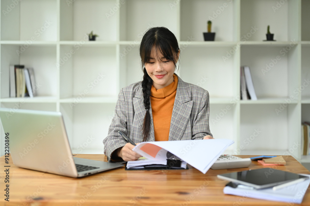Asian female financier worker using laptop and checking statistic report at office desk Asian female financier worker using laptop and checking statistic report at office desk