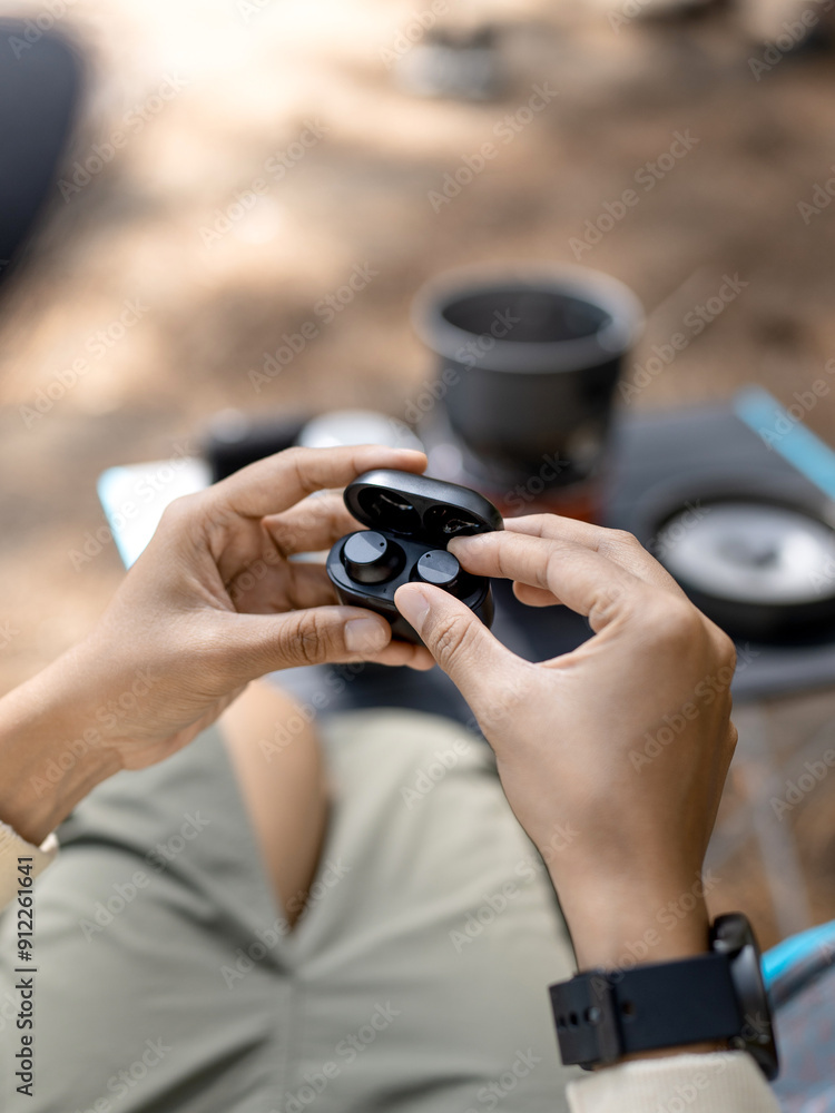 close up of a person holding a wireless earphone case while camping in nature close up of a person holding a wireless earphone case while camping in nature