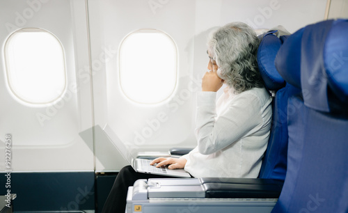 senior woman sitting on an airplane with her head in her hands. Asian woman sitting