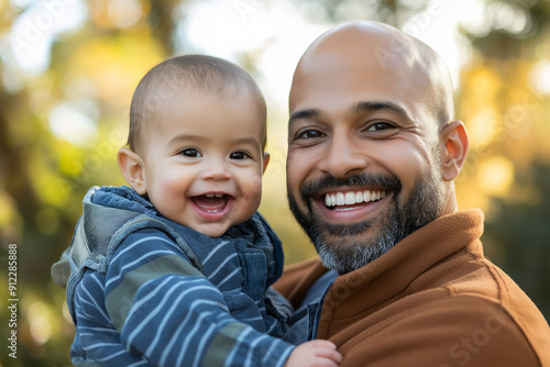 A happy bald father holding his smiling baby in an outdoor park, symbolizing fatherhood and joy.