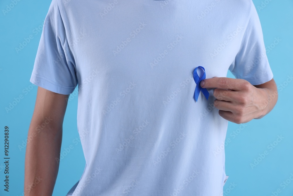 Prostate cancer awareness. Man with blue ribbon as symbol of support on color background, closeup Prostate cancer awareness. Man with blue ribbon as symbol of support on color background, closeup
